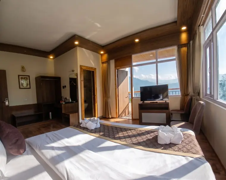 Room with an open balcony door and a television, hills visible outside